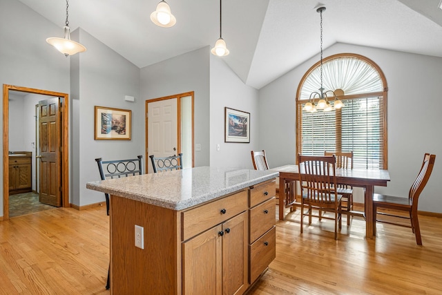 kitchen featuring pendant lighting, a center island, light stone countertops, light hardwood / wood-style floors, and vaulted ceiling