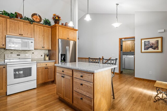 kitchen with decorative light fixtures, a kitchen island, white appliances, washer and clothes dryer, and light hardwood / wood-style floors