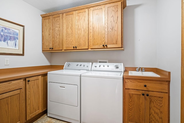 clothes washing area with sink, washing machine and dryer, and cabinets