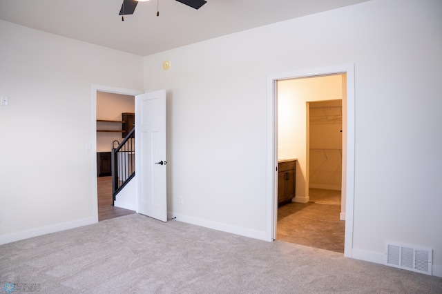 unfurnished bedroom featuring a spacious closet, light colored carpet, and ceiling fan