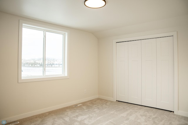 unfurnished bedroom featuring lofted ceiling, light carpet, and a closet