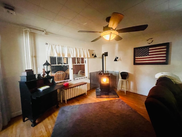 bedroom featuring ceiling fan, radiator, hardwood / wood-style floors, and a wood stove