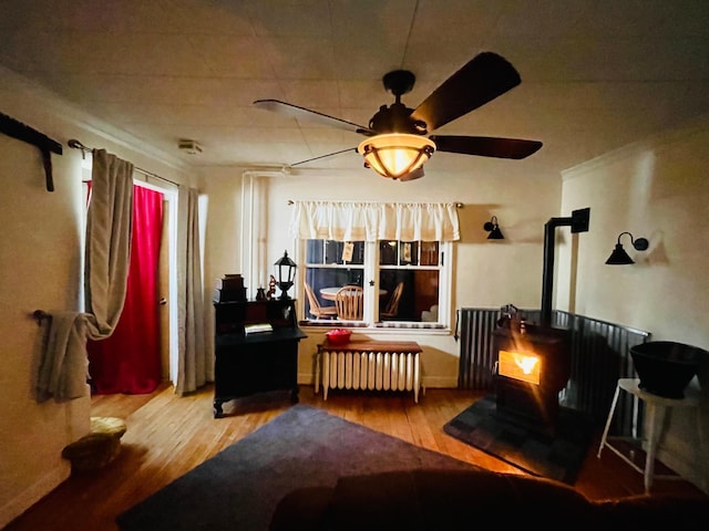 living area featuring radiator heating unit, light hardwood / wood-style floors, ceiling fan, and a wood stove