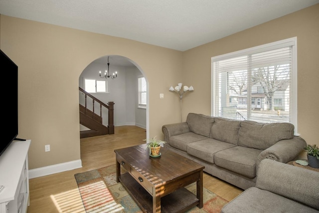 living room with arched walkways, a chandelier, baseboards, stairway, and light wood-type flooring