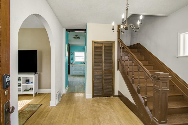 stairway featuring visible vents, a notable chandelier, baseboards, and wood finished floors