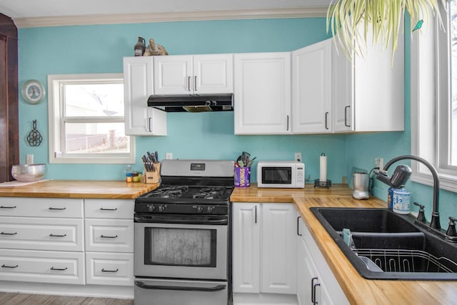 kitchen with under cabinet range hood, stainless steel range with gas cooktop, wooden counters, and white microwave