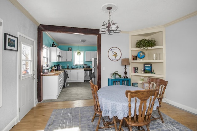 dining space featuring light wood-type flooring, baseboards, ornamental molding, and a notable chandelier