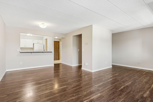 unfurnished living room featuring a textured ceiling, dark wood-type flooring, and baseboards