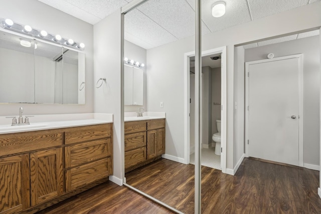 bathroom with toilet, wood finished floors, two vanities, a sink, and baseboards