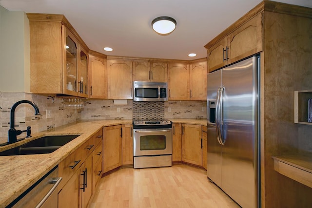 kitchen featuring sink, light wood-type flooring, appliances with stainless steel finishes, light stone countertops, and decorative backsplash