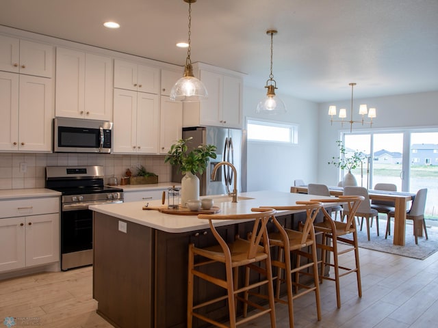 kitchen with a breakfast bar, decorative light fixtures, an island with sink, white cabinetry, and stainless steel appliances