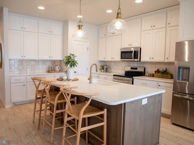 kitchen with an island with sink, appliances with stainless steel finishes, sink, and white cabinets