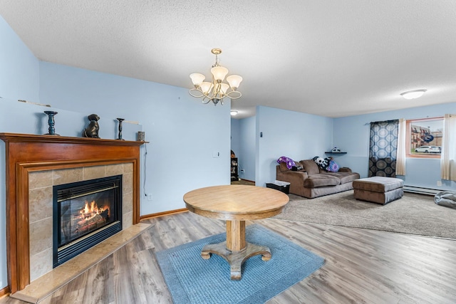 living room with a baseboard heating unit, a textured ceiling, a tile fireplace, and light hardwood / wood-style flooring