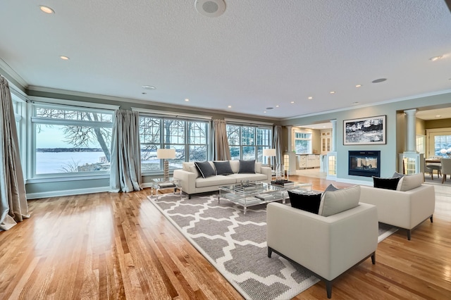 living room with crown molding, a textured ceiling, light hardwood / wood-style flooring, and ornate columns