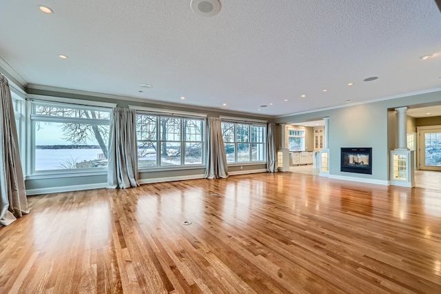 unfurnished living room with crown molding, decorative columns, a multi sided fireplace, light hardwood / wood-style floors, and a textured ceiling