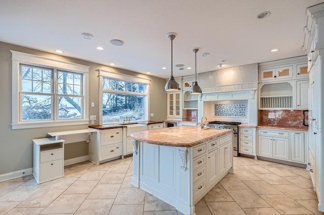 kitchen with tasteful backsplash, decorative light fixtures, an island with sink, high end stainless steel range oven, and white cabinets