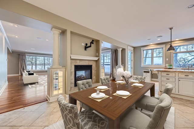 dining space featuring ornate columns, a tile fireplace, light tile patterned floors, and crown molding