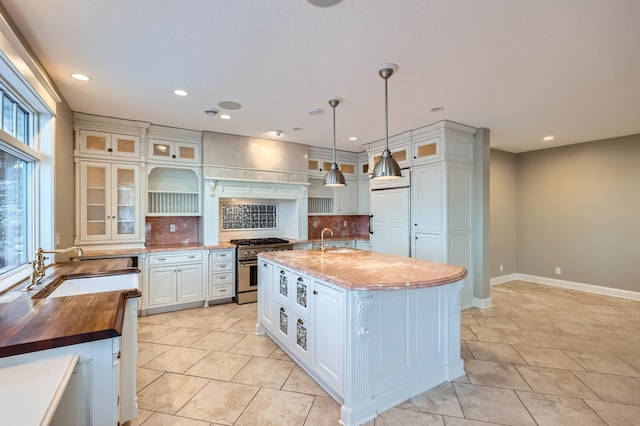 kitchen featuring sink, hanging light fixtures, dark stone countertops, premium appliances, and an island with sink