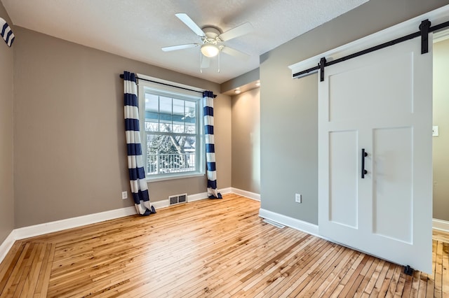 spare room featuring ceiling fan, a barn door, light hardwood / wood-style floors, and a textured ceiling