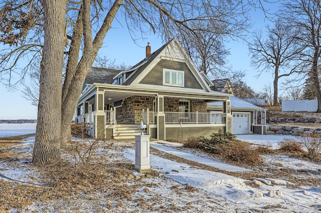 shingle-style home with a garage, stone siding, a porch, and a chimney