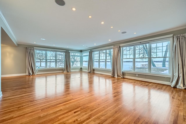 unfurnished living room featuring a healthy amount of sunlight, crown molding, baseboards, and wood finished floors