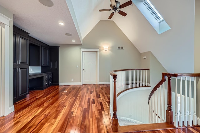 interior space featuring visible vents, an upstairs landing, light wood-type flooring, vaulted ceiling with skylight, and baseboards