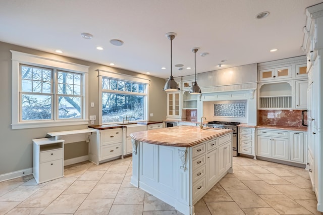 kitchen featuring an island with sink, glass insert cabinets, high end stainless steel range, open shelves, and backsplash