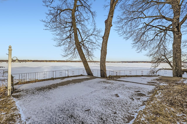 snowy yard with a water view and a fenced backyard