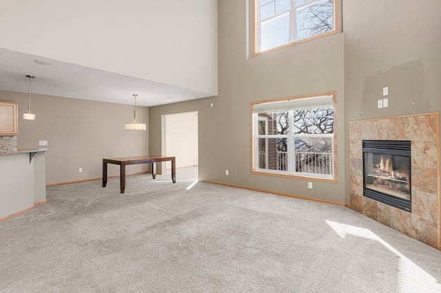 unfurnished living room with a tiled fireplace, light carpet, and a wealth of natural light