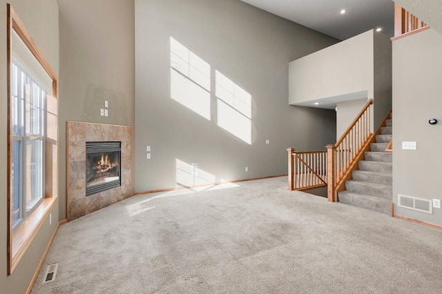 unfurnished living room with carpet floors, a fireplace, and a towering ceiling