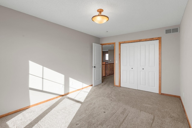 unfurnished bedroom with light colored carpet, a textured ceiling, and a closet