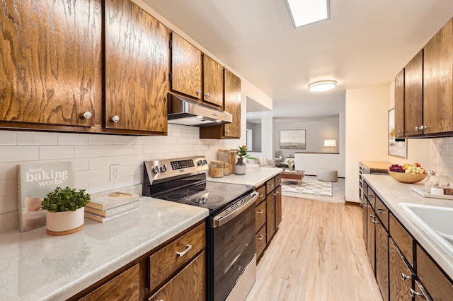 kitchen with electric range, decorative backsplash, light wood-style floors, light countertops, and under cabinet range hood