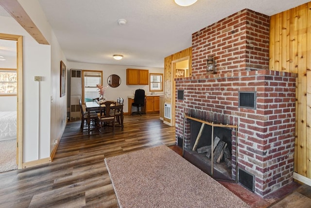 living room featuring a textured ceiling, wood walls, baseboards, a brick fireplace, and dark wood-style flooring