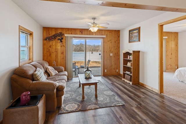 living room featuring a textured ceiling, wood finished floors, wood walls, baseboards, and ceiling fan