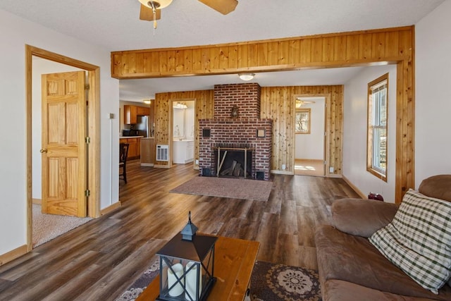 living area with a brick fireplace, baseboards, ceiling fan, wood walls, and dark wood-style floors