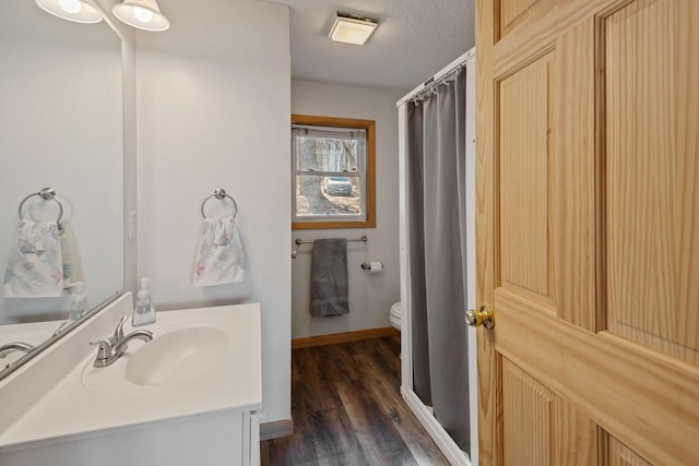 bathroom with toilet, a textured ceiling, wood finished floors, baseboards, and vanity