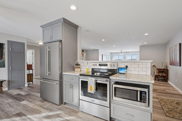 kitchen with gray cabinetry, light stone countertops, stainless steel appliances, and light wood-type flooring