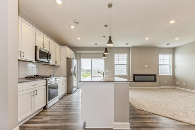 kitchen with tasteful backsplash, decorative light fixtures, a center island with sink, stainless steel appliances, and white cabinets