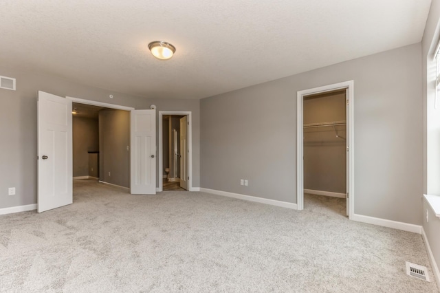 unfurnished bedroom featuring a walk in closet, light carpet, a textured ceiling, and a closet