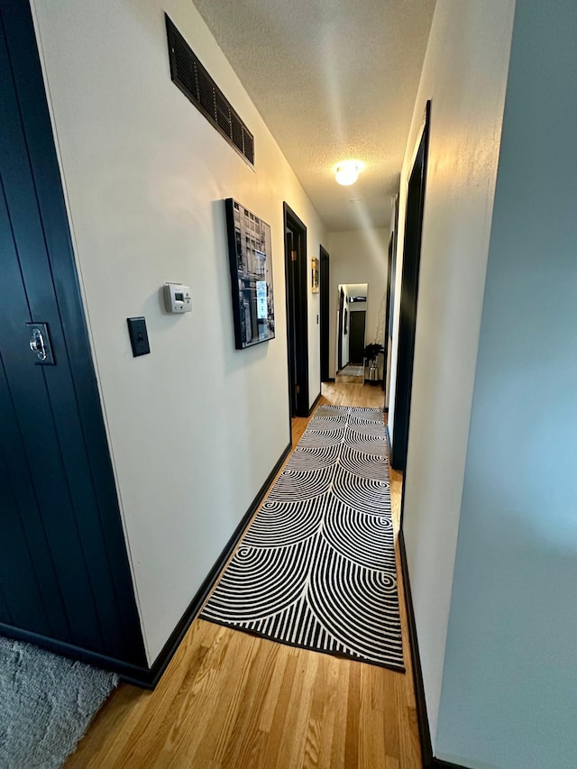 hall featuring a textured ceiling and light hardwood / wood-style floors