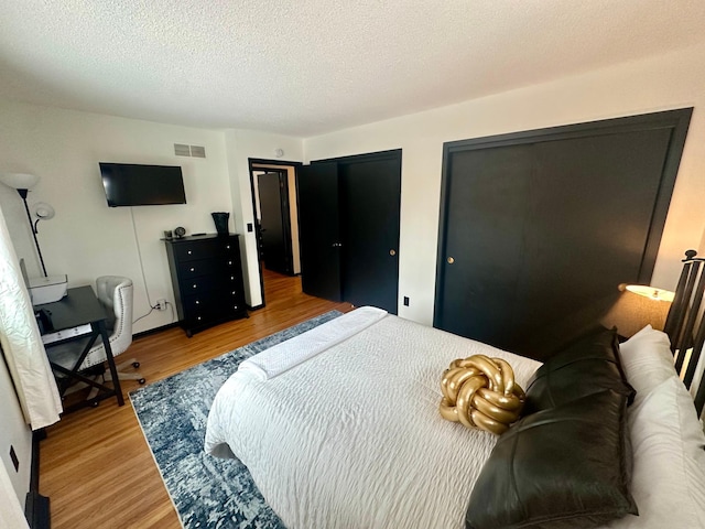 bedroom with two closets, a textured ceiling, and light hardwood / wood-style floors