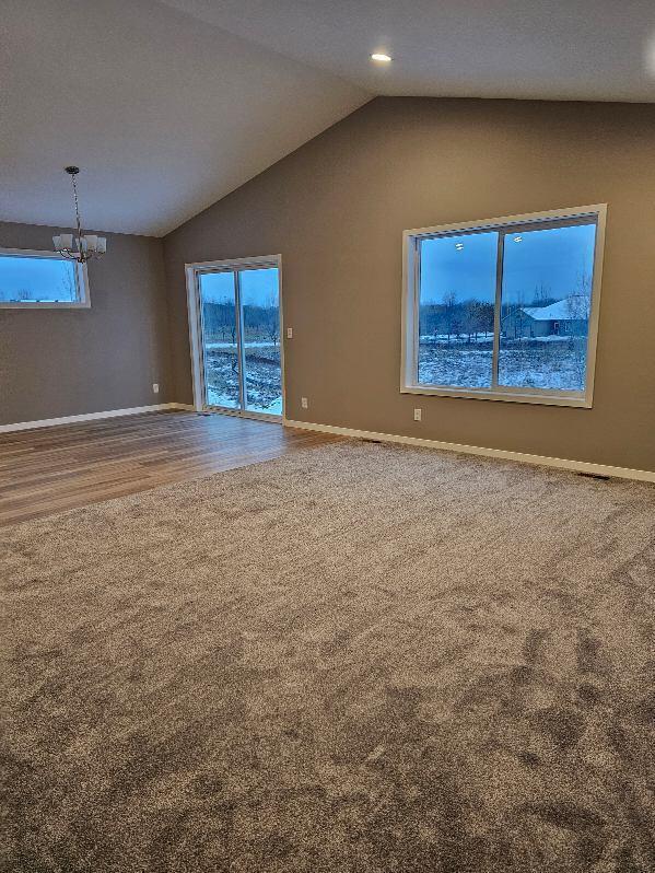 spare room featuring vaulted ceiling, carpet floors, and an inviting chandelier