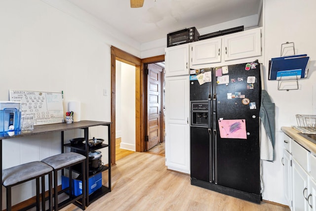 kitchen with light wood-type flooring, ceiling fan, white cabinetry, and black fridge with ice dispenser