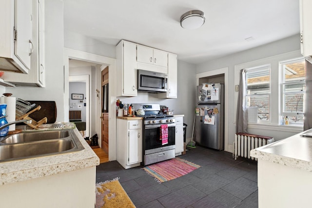 kitchen featuring radiator heating unit, appliances with stainless steel finishes, light countertops, white cabinetry, and a sink