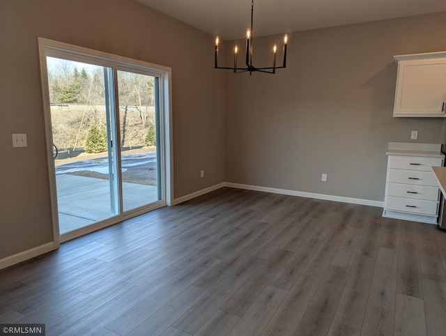 unfurnished dining area featuring a chandelier, baseboards, and wood finished floors