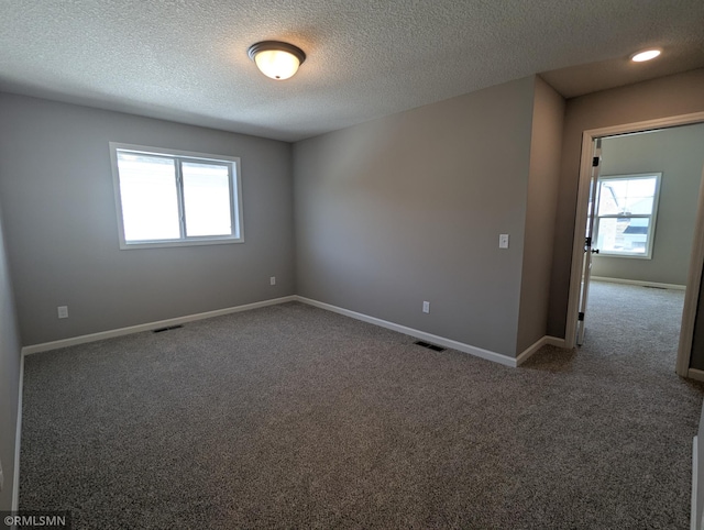 carpeted spare room featuring visible vents, baseboards, and a textured ceiling