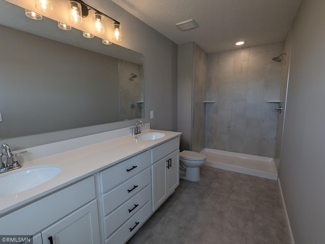 full bathroom featuring a sink, tiled shower, toilet, and double vanity