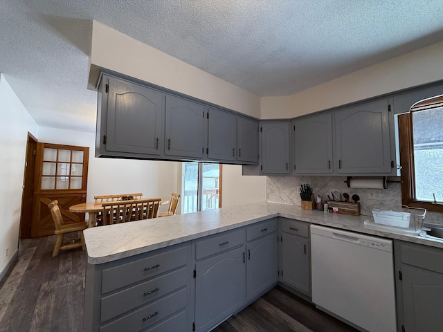 kitchen featuring gray cabinetry, dark hardwood / wood-style floors, dishwasher, kitchen peninsula, and backsplash