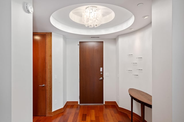 hall with a tray ceiling, hardwood / wood-style floors, and a notable chandelier