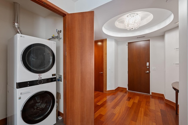 clothes washing area with hardwood / wood-style floors, stacked washer and clothes dryer, and a chandelier